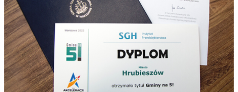 Na stole ułożone są kolejno, list przewodni, granatowa teczka szkoły Głównej Handlowej a na wierzchu dyplom Gmina na 5 dla Miasta Hrubieszów 