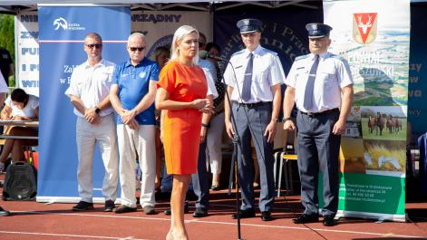 Burmistrz Miasta Marta Majewska przemawia przez mikrofon, za nią stoją mężczyźni w mundurach