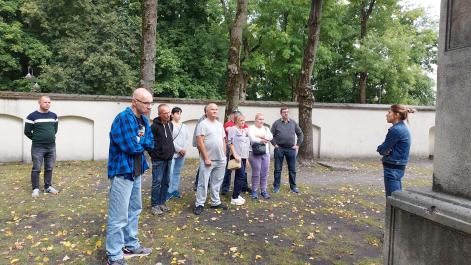 Uczestnicy stoją przezd kobietą, która coś im opowiada