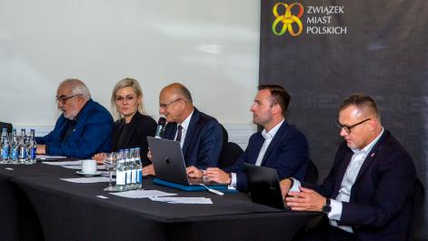 Zarząd siedzi za stołem prezydialnym, jedna osoba mówi do mikrofonu