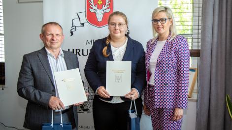Marta Majewska, zawodniczka w podnoszeniu ciężarów oraz jej trener pozują do zdjęcia. w rękach mają teczki z herbem miasta oraz pamiątkowe upominki 