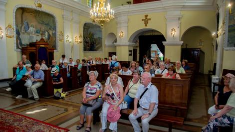 Seniorzy siedzą w ławkach, słuchają przemowy