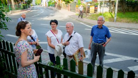 Kobieta opowiada osobom stojącym przed płotem przy Zinówce