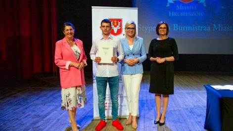 Kobiety oraz stypendysta pozują do zdjęcia, w tle widać roll-up z herbem miasta Hrubieszów