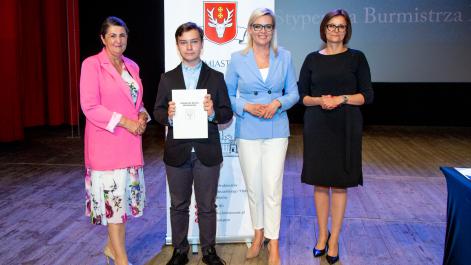 Kobiety oraz stypendysta pozują do zdjęcia, w tle widać roll-up z herbem miasta Hrubieszów