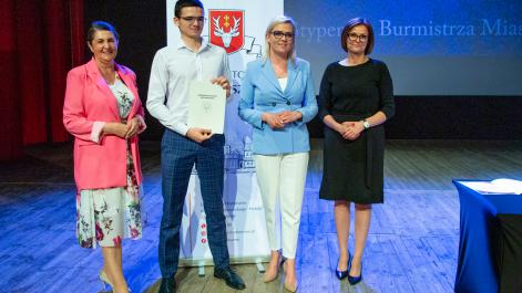 Kobiety oraz stypendysta pozują do zdjęcia, w tle widać roll-up z herbem miasta Hrubieszów