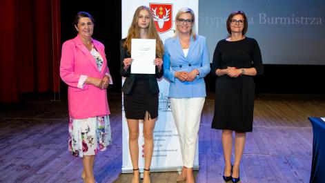Kobiety oraz stypendystka pozują do zdjęcia, w tle widać roll-up z herbem miasta Hrubieszów