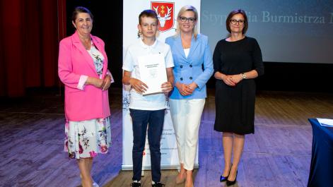 Kobiety oraz stypendysta pozują do zdjęcia, w tle widać roll-up z herbem miasta Hrubieszów