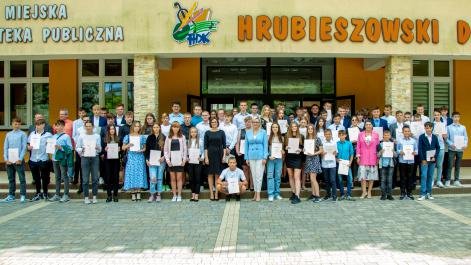 Zdjęcie grupowe wszyscy stypendyći stoją przed budynkiem Hrubieszowiskiego Domu Kultury w rękach trzymają teczki z herbem miasta, pozują z nimi kobiety, które wręczały nagrody