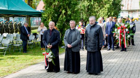 Księża, jeden z nich trzyma kwiaty