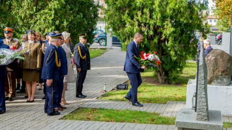 Mężczyzna podąża w stronę pomnika, w rękach trzyma kwiaty