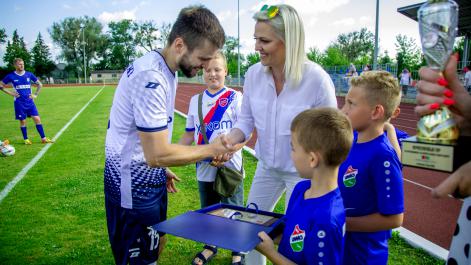 Burmistrz gratuluje kapitanowi drużyny gości udanego meczu, chłopiec stojący obok trzyma w rękach pamiątkowy grawerunek