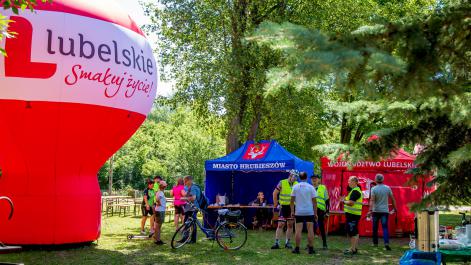 Trwa piknik po rajdzie, ludzie stoją przy namiocie promocyjnym