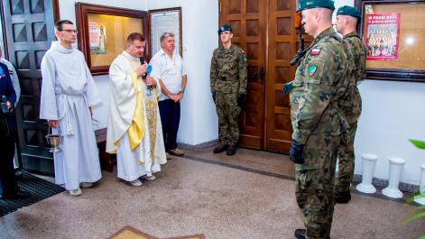 Ksiądz stoi naprzeciw żołnierzy trzymających wartę, trwa modlitwa