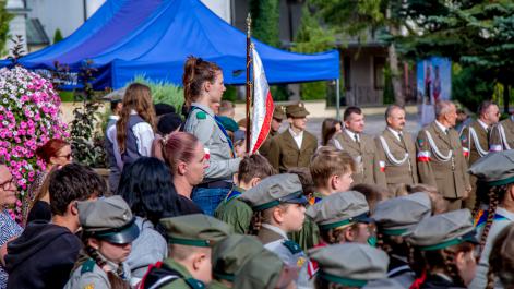 wśród siedzących harcerzy jedna z nich stoi ze sztandarem